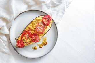 Half eggplant baked with turmeric, ginger, onions, tomatoes and sesame seed on a plate, healthy