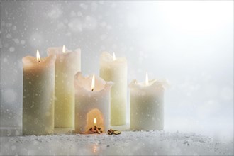 White candles burning in the snow, in one is a carve with a warm campfire, surreal winter still