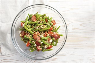 Antipasto salad of green beans, tomatoes, pine nuts and feta cheese in a glass bowl on a light