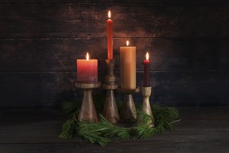 Four different candles in warm colors on wooden stands for Advent with some pine branches against a