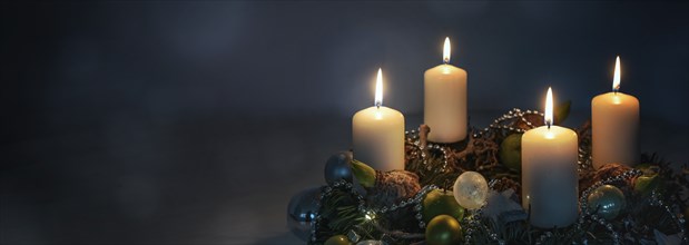 Lights in the night, four white Advent candles on a wreath with Christmas decoration against a dark