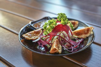 Deep fried gyoza with salad and sauce served as appetizer on a black plate, Asian dish on a wooden