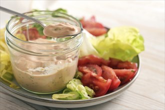 Salad dressing from skyr on a spoon and in a glass jar on a plate with slices of lettuce and