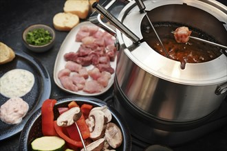 German fondue with raw meat and vegetables to be fried on long forks in a pot with boiling oil,