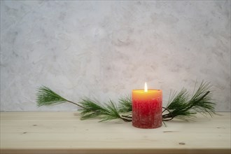 Red candle lit for the first Advent, pine branch as a simple, minimal decoration on a light wooden