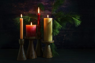 Advent arrangement with four candles in red and yellow on wooden holders and pine branches against