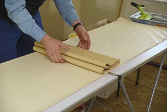 A man rolls up some glued wallpaper, ready to decorate a bedroom