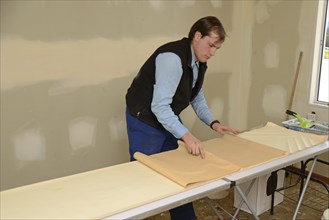 A man rolls up some glued wallpaper, ready to decorate a bedroom