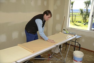 A man rolls up some glued wallpaper, ready to decorate a bedroom