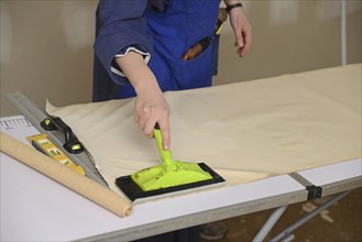 A woman spreads glue on the back of wallpaper, ready to decorate a bedroom