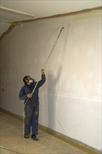 A tradesman using airless spray equipment to paint a top coat on the walls of a commercial building