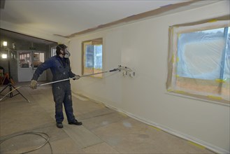 A tradesman using airless spray equipment to paint a top coat on the walls of a commercial building