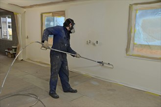 A tradesman using airless spray equipment to paint a top coat on the walls of a commercial building