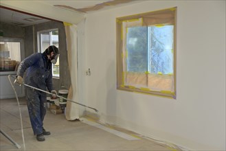 A tradesman using airless spray equipment to paint a top coat on the walls of a commercial building