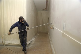 A tradesman using airless spray equipment to paint a top coat on the walls of a commercial building