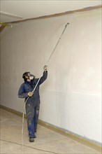 A tradesman using airless spray equipment to paint a top coat on the walls of a commercial building