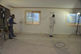 A tradesman using airless spray equipment to paint a top coat on the walls of a commercial building