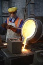 A foundryman pours molten iron into molds for making fire grates. (Shot in available light with