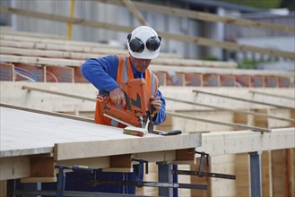 A builder uses a nail gun to secure timber on the verandah of new building