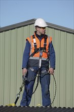 A builder wearing a safety harness while working at heights waits for instructions from the foreman