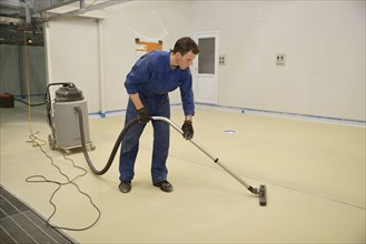 Tradesman vacuums floor of an industrial building in preparation for painting