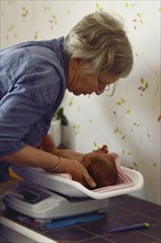 A senior midwife weighs a young baby as part of her post-natal check