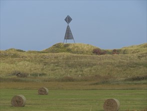 Rural landscape with hay bales and a monument in a meadow under a cloudy sky, Juist, East Frisia,