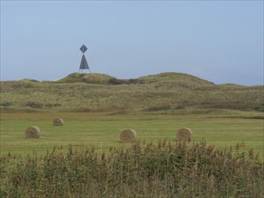 A wide field with hay bales in the foreground and dunes and a tower in the background, Juist, East