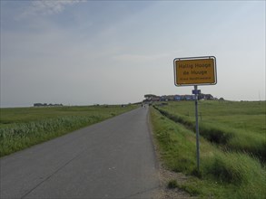 Rural road with a sign and a meadow, in the background buildings and a wide sky, Hallig Hooge,