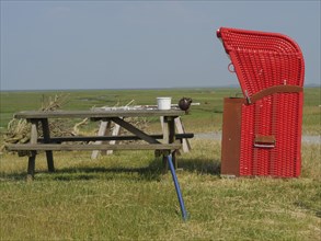 A red beach chair and a picnic table stand in a meadow under a clear sky, the surroundings are