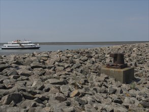 A ferry sails along a rocky coast under a clear sky, the scene looks industrial and natural at the