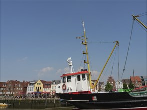 A harbour with a large boat in the foreground and colourful houses in the background under a blue