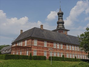 Large historic brick building with tower and windows on a green meadow under a blue sky, husum,