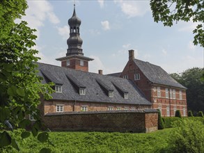 Historic building with church tower and tiled roof surrounded by green plants under a blue sky,