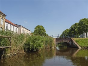 An idyllic canal with an old stone lock and surrounded by green trees and traditional buildings on