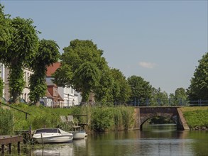 Idyllic scene of a canal with a small bridge, surrounded by trees and houses, friedrichstadt,