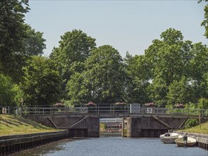 A bridge over a canal, surrounded by green trees and boats on the bank, summer atmosphere,