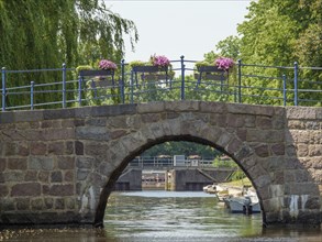 Historic stone bridge over a canal with flowers and boats in the water on a sunny day,