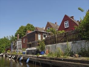 Houses with wooden fences along the canal with boats in the water and green vegetation,