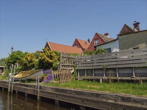 Cosy scene with boat and garden at the canal, wooden benches and blooming flowers, sunny day,