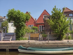 House on the canal with red roofs, surrounded by green trees and a boat in the foreground,