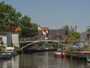 An idyllic scene with a bridge over a canal, surrounded by boats, houses and trees under a clear