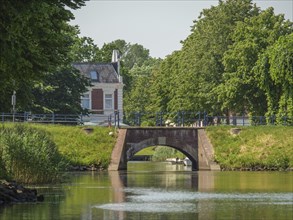 A historic bridge spans a river, lined with trees and a green landscape, friedrichstadt,