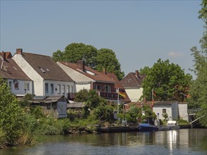 Various houses and boats along a quiet riverbank, surrounded by trees and vegetation,