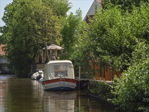 A white and red boat lies on a riverbank against a green, overgrown backdrop, friedrichstadt,