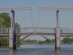 Modern metal bridge spans a river under a blue sky with green surroundings, friedrichstadt,