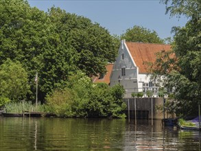 A white house with red roof tiles stands on the riverbank, surrounded by lush vegetation,