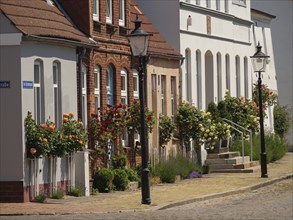 Blooming flowers in front of historic houses and street lamps along a cobbled street,