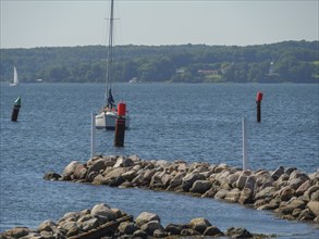 A harbour with a sailing boat, buoys and a rocky shore under a blue sky in summer, Flensburg,