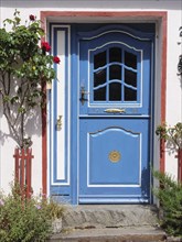 Blue decorated entrance door of a house, surrounded by blooming flowers and decorative elements,